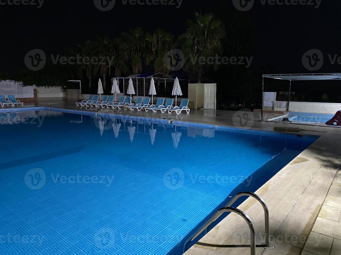 Beautiful night swimming pool with umbrellas and deck chairs and palm trees in a hotel on vacation in a tourist warm tropical eastern country southern resort photo