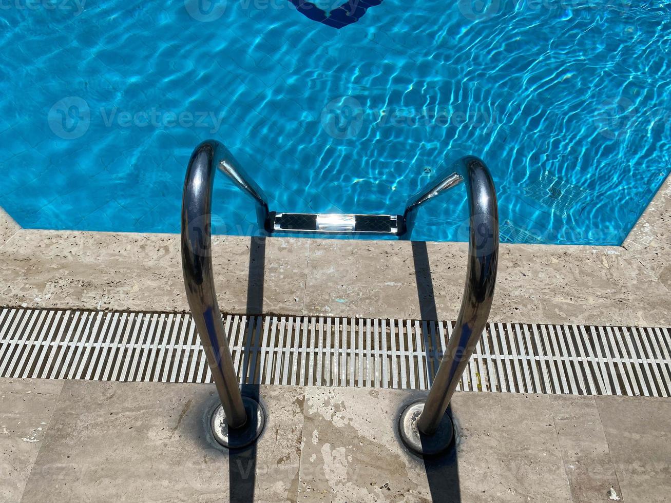 Frontal view of a ladder for entering in a crystal clear blue swimming pool water photo