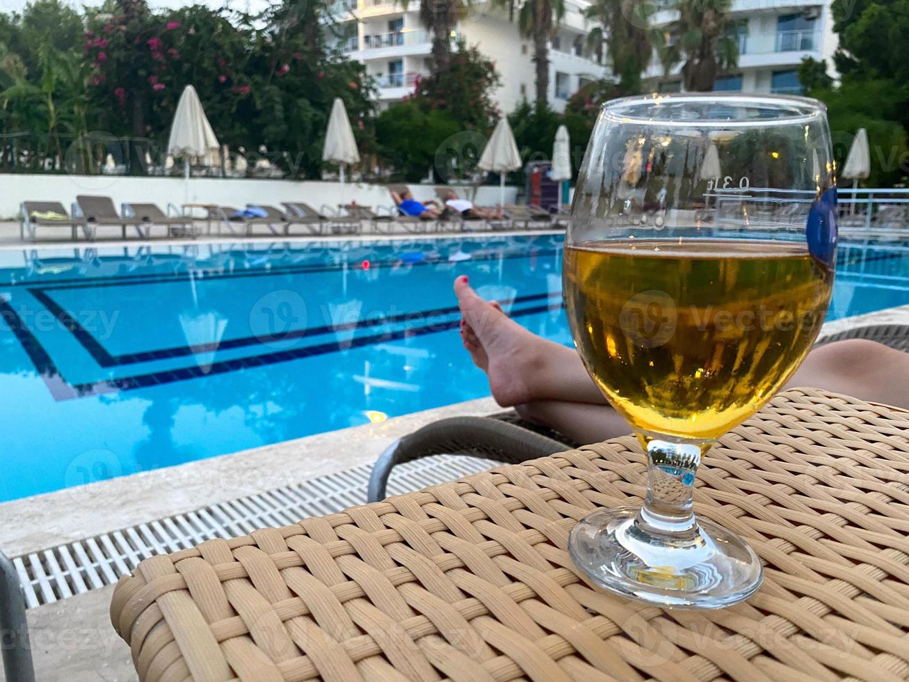 copa de vidrio de cerveza helada fresca y deliciosa frente a la piscina de vacaciones en un resort tropical foto