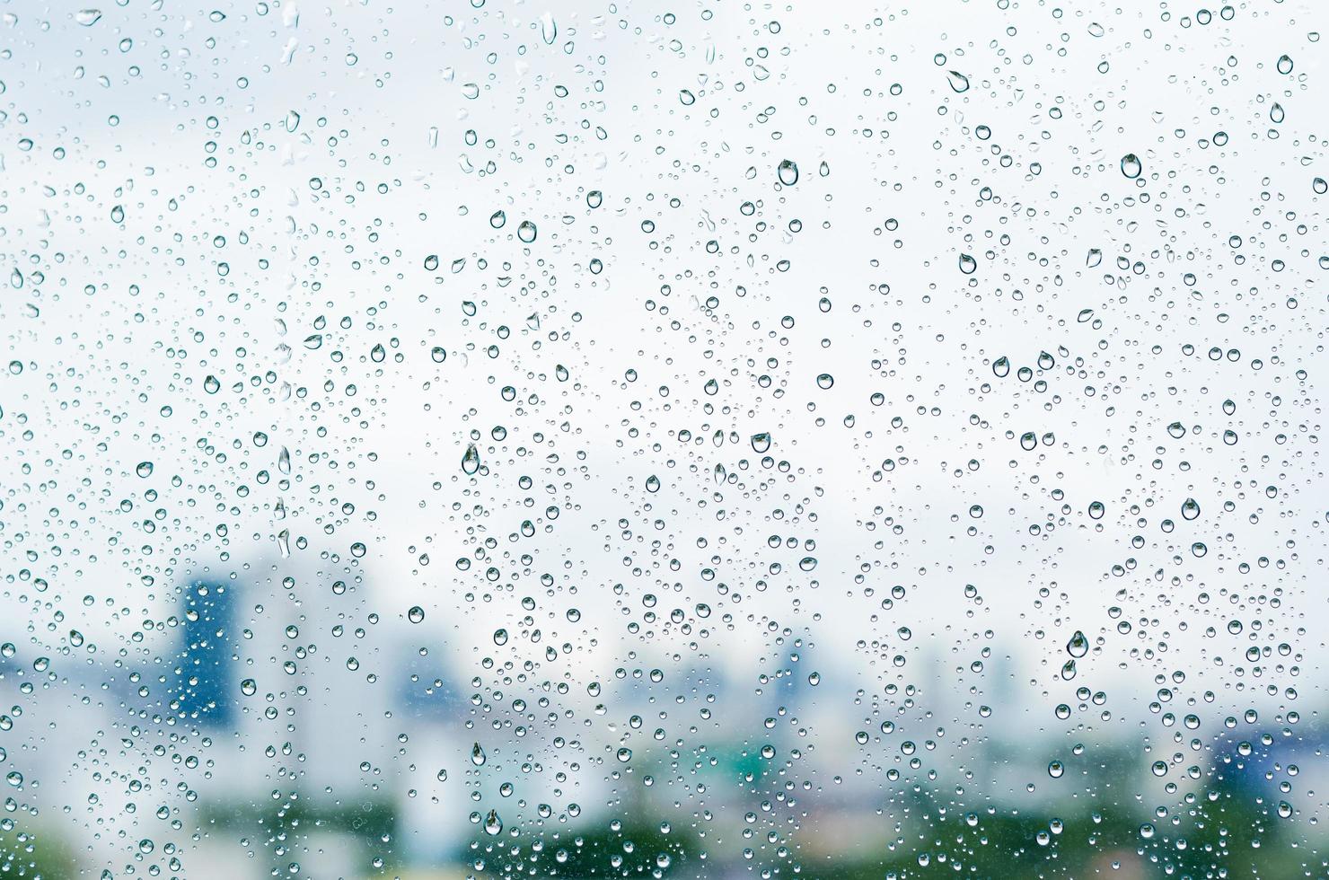 Rain drop on glass window at day time in monsoon season with blurred city buildings background. photo
