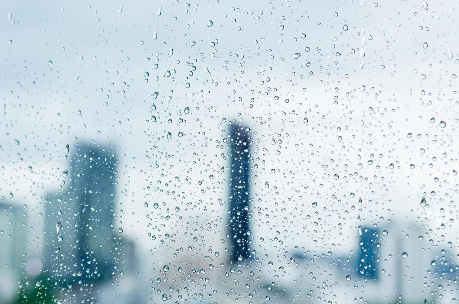 Rain drop on glass window at day time in monsoon season with blurred city buildings background. photo