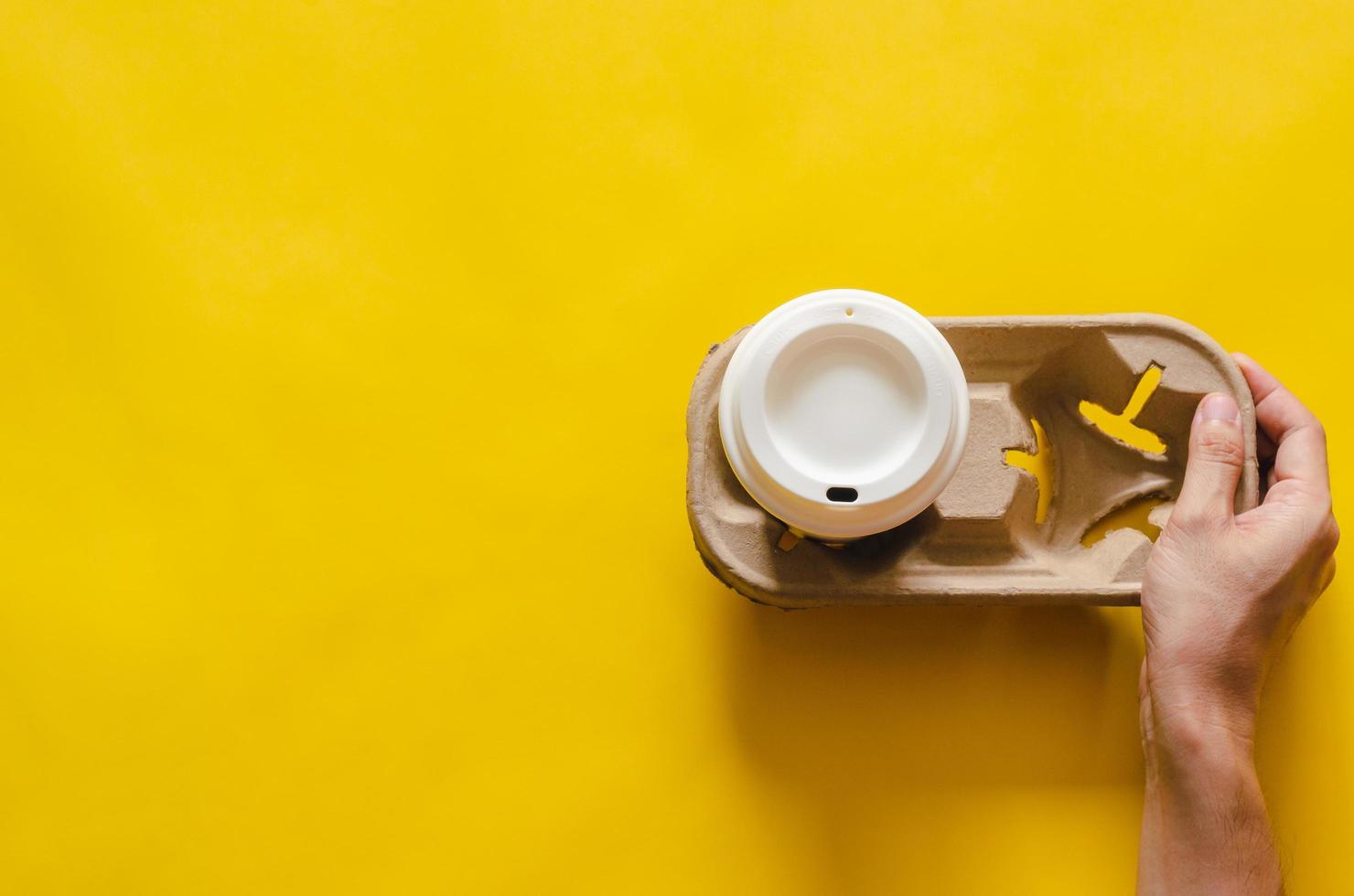 Hand holding reuse paper tray with a recycle cup of coffee on yellow paper background for World environment concept. photo