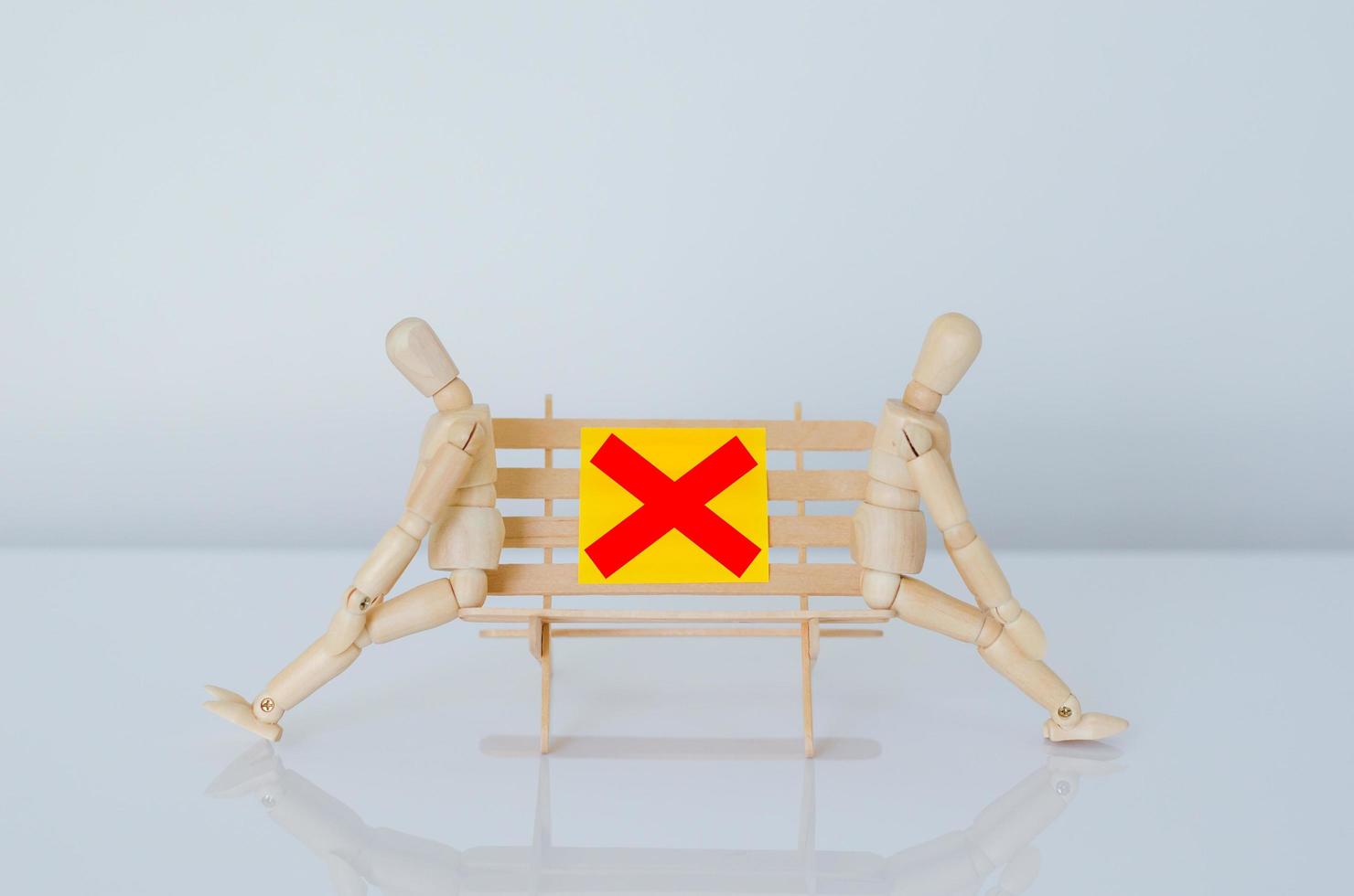 Two wood models sitting on bench and keep distance with the gap to protect flu infection. photo