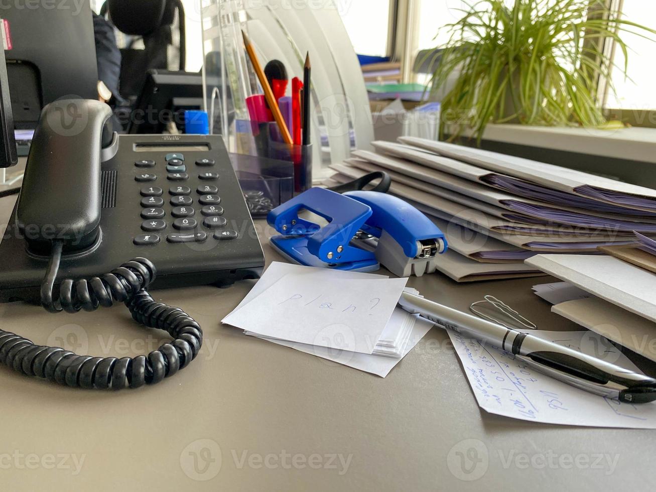 Black landline telephone with a tube, buttons and a wire on the work table at the office desk with office supplies. Business work photo