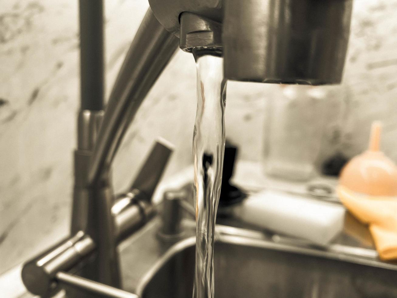 un chorro de agua limpia, fría y transparente filtrada fluye de un grifo de hierro sanitario cromado, un grifo en la cocina del apartamento foto