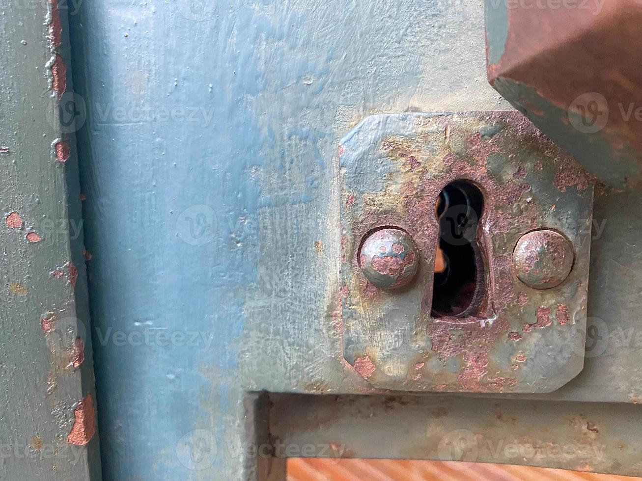 Old rusty ancient iron metal keyhole for opening with a key on a door painted with blue paint photo