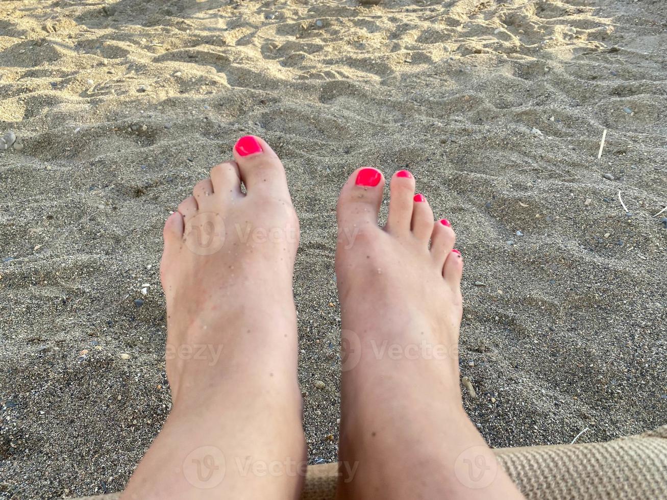 Female legs, feet with a beautiful red pedicure on the background of sand on vacation on the beach in a warm tropical eastern paradise country southern resort photo