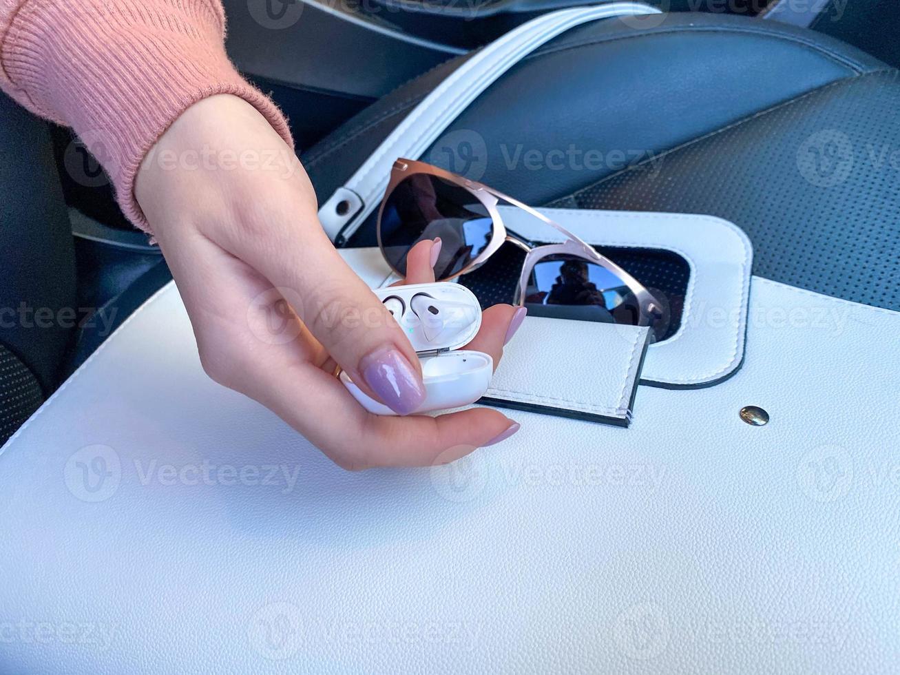 White female beautiful fashionable leather bag and sunglasses with wireless headphones and female hand in the car photo