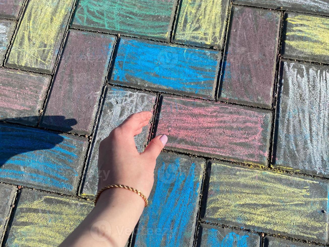 Beautiful female hands with fingers and a beautiful pink manicure against the background of paving slabs painted with children's colorful bright crayons photo