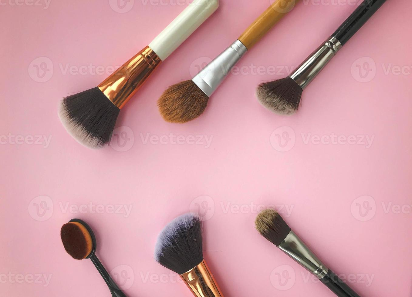 Beautiful fashionable beauty cosmetic glamorous white and gold brushes and brushes for applying makeup and powder and cosmetics on the face on a pink gentle background. Flat lay photo