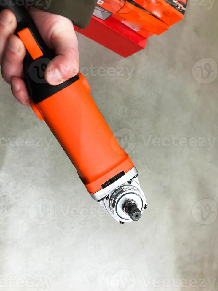 red construction tool. a man holds a tool for repair and housework with a strong hand. DIY repair. screwing into the surfac photo