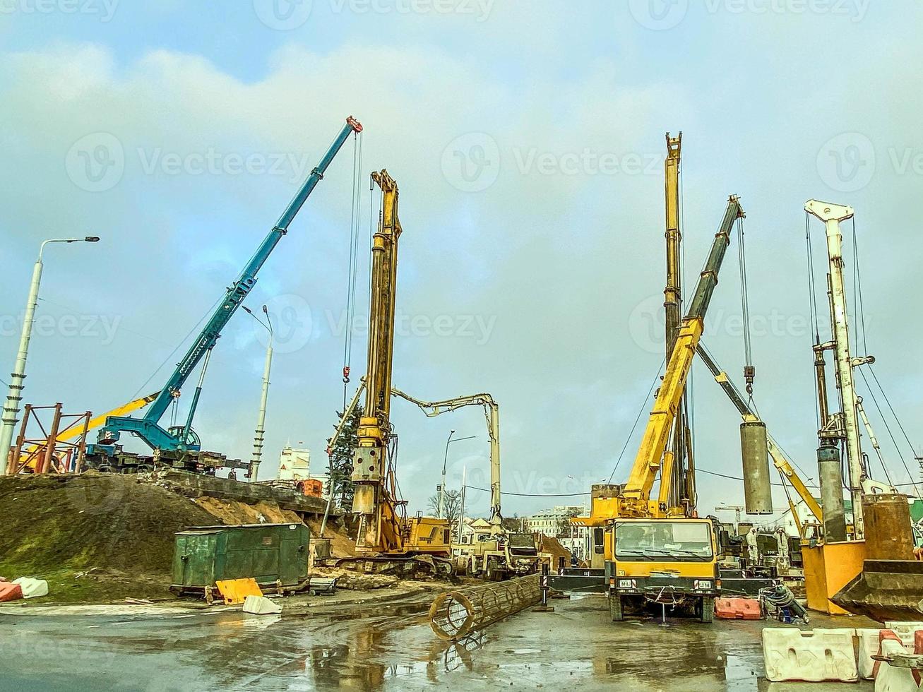 construction equipment at the overpass repair site. large concrete blocks are erected by cranes. next to a large truck. construction site in the rain with puddles photo