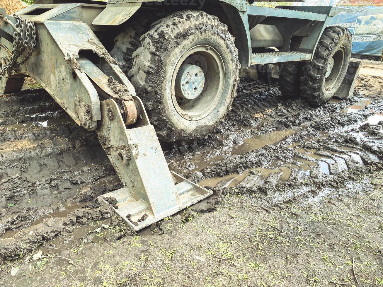 a tractor with large, black wheels in the mud. metal anchor to hold the machine in place. black wheel stuck in a puddle of mud photo