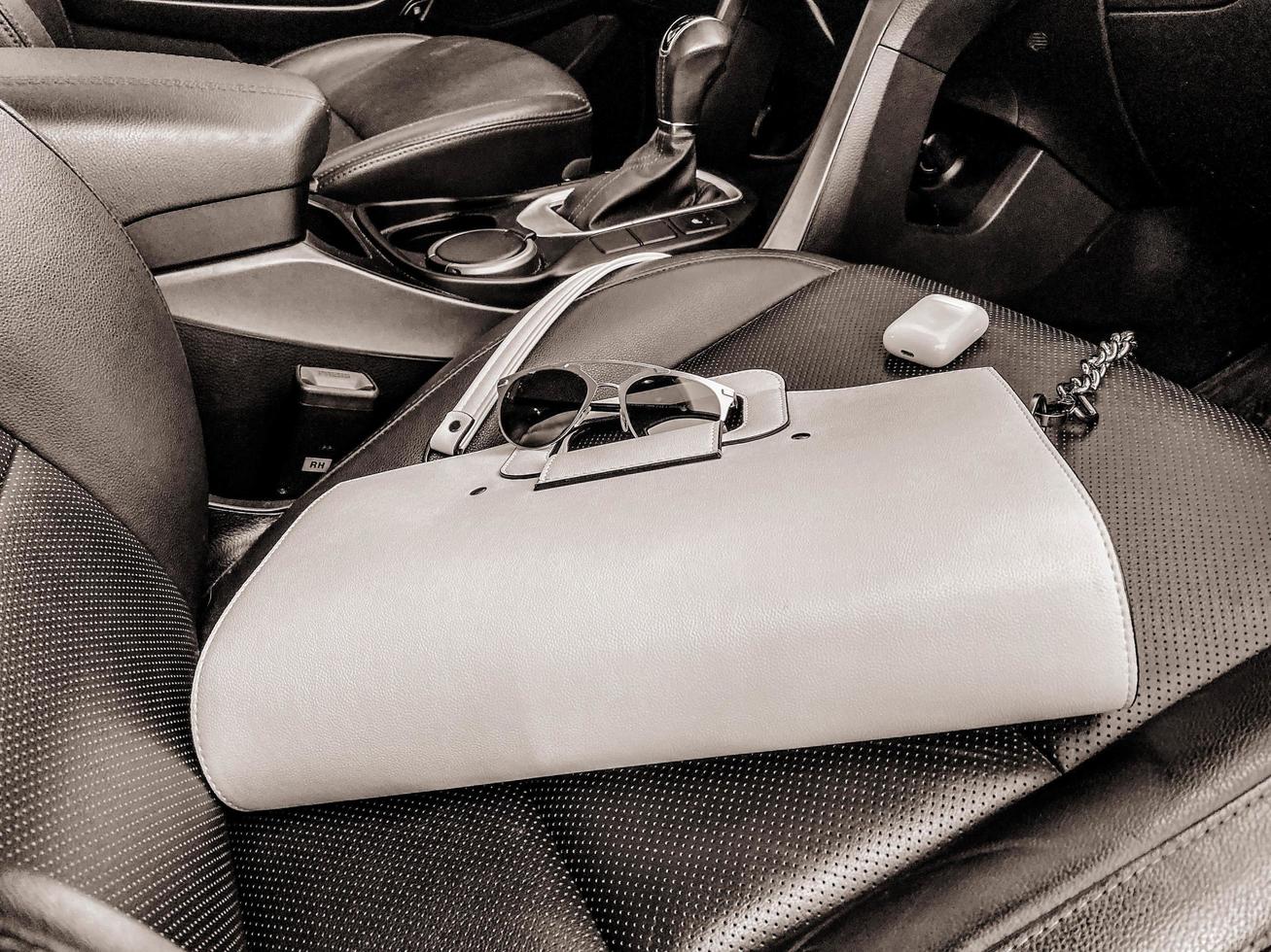 White women's beautiful fashionable leather bag and sunglasses with wireless headphones lie on the leather armchair of a good expensive car photo