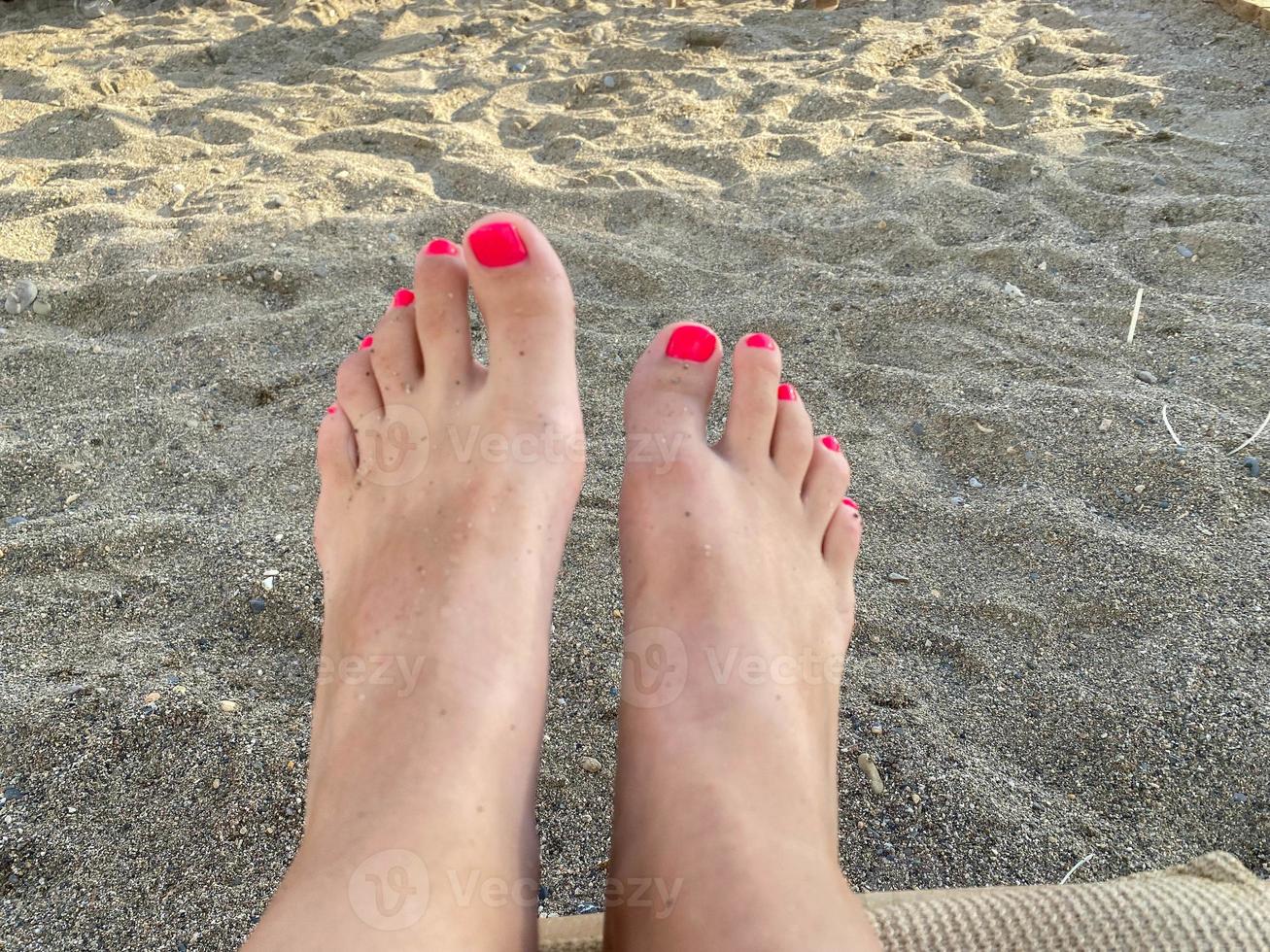 Female legs, feet with a beautiful red pedicure on the background of sand on vacation on the beach in a warm tropical eastern paradise country southern resort photo