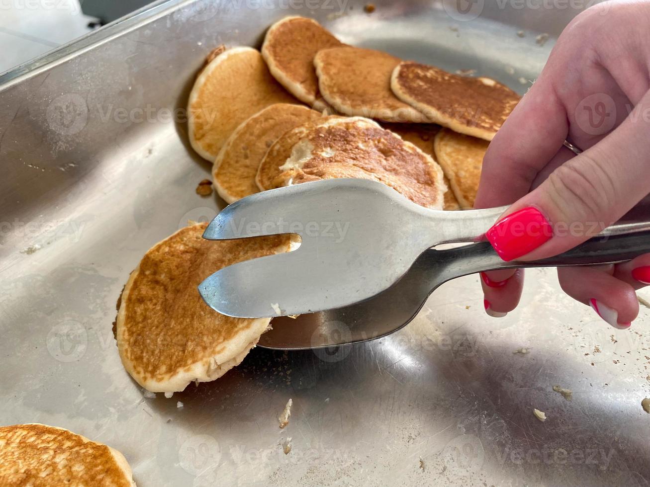 una hermosa mano de una niña toma con pinzas deliciosos panqueques de harina para el desayuno de un plato en un café cantina. el fondo. textura foto