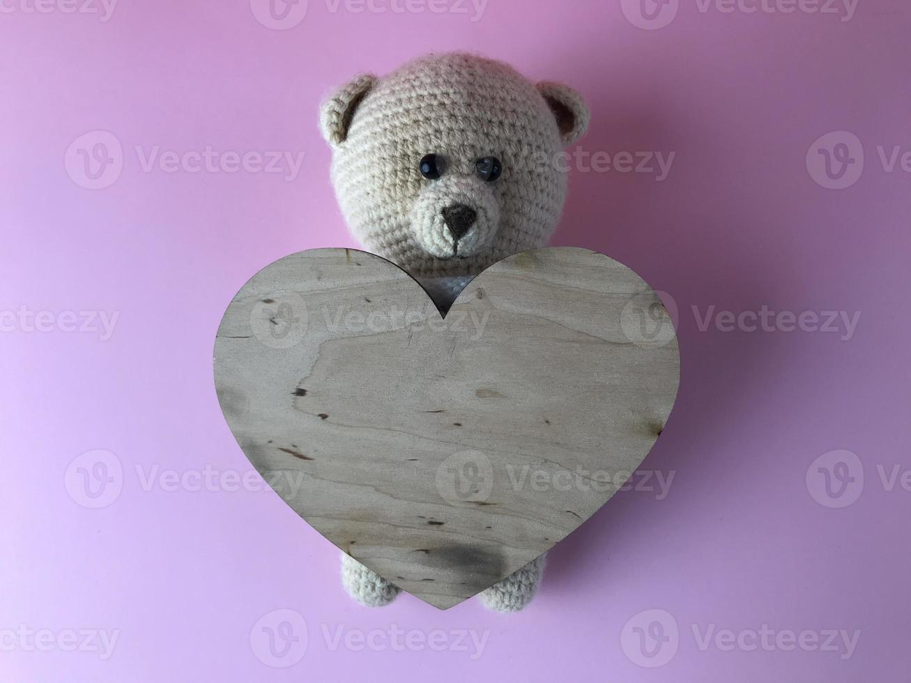 knitted bear with a heart made of wood. cute gift on a pink background. an engagement gift. handmade bear of threads, crocheted photo