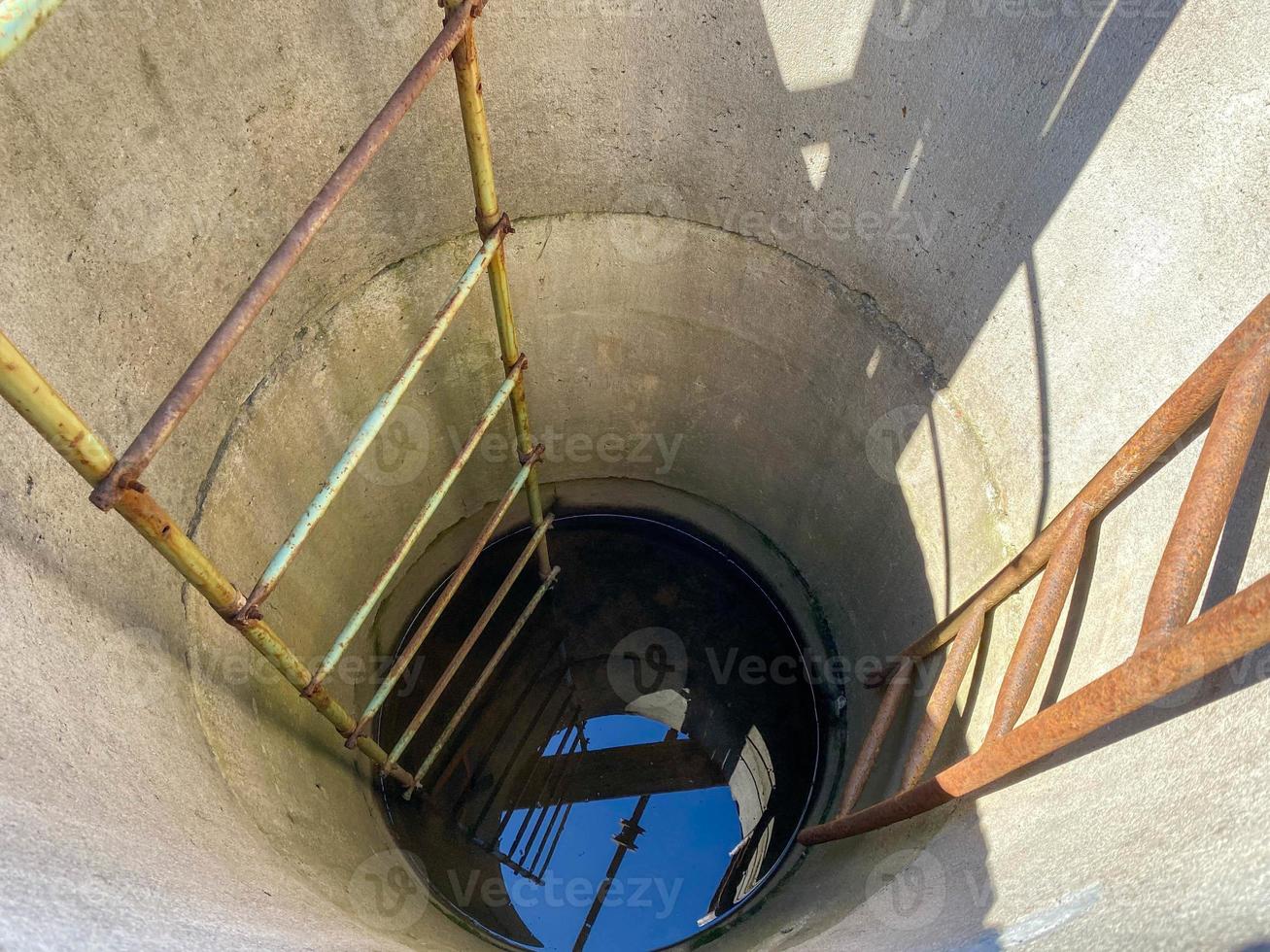 A large round deep well made of concrete rings with clean well underground water for drinking with old rusty stairs photo