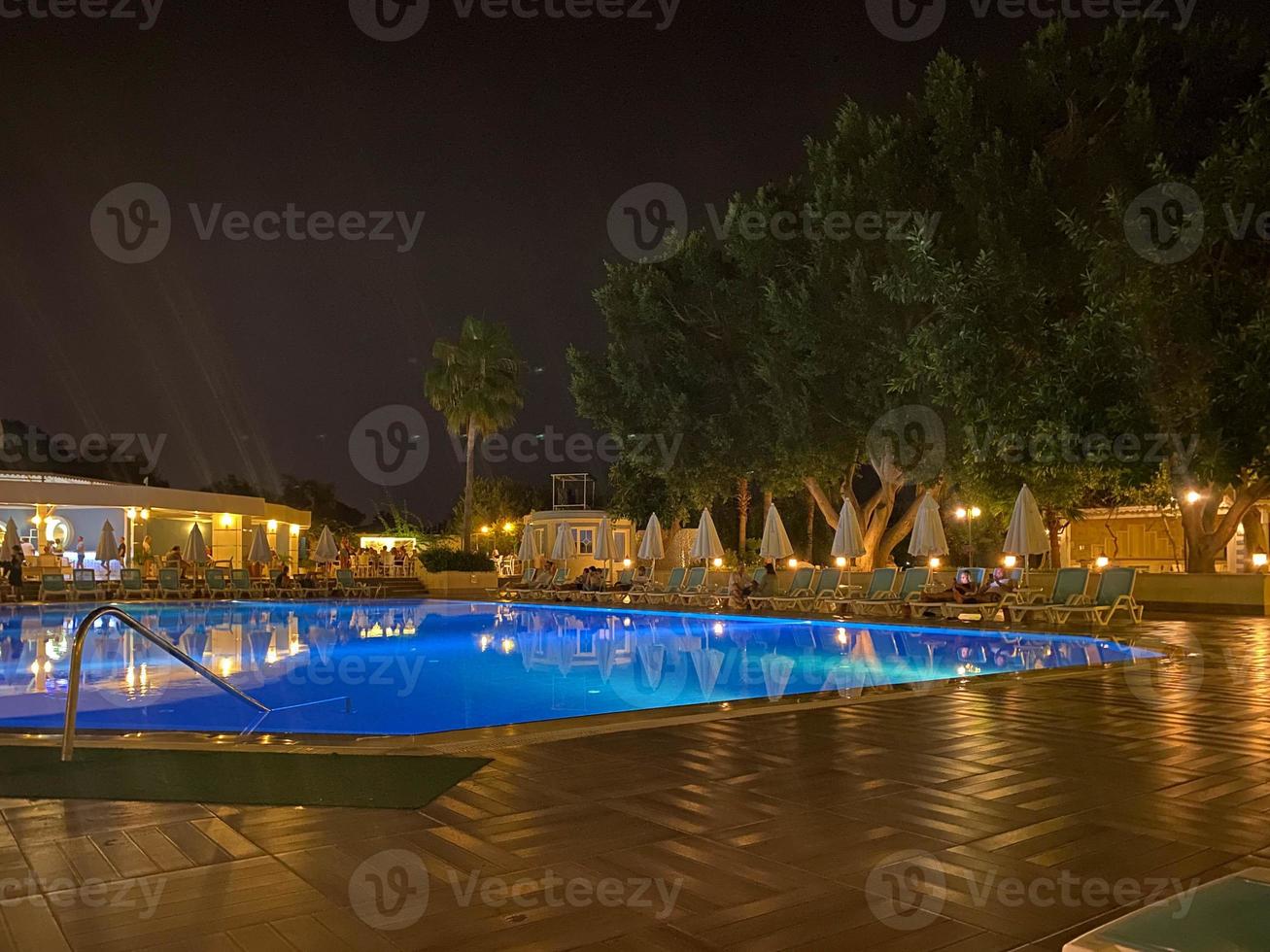 Beautiful night swimming pool with umbrellas and deck chairs and palm trees in a hotel on vacation in a tourist warm tropical eastern country southern resort photo