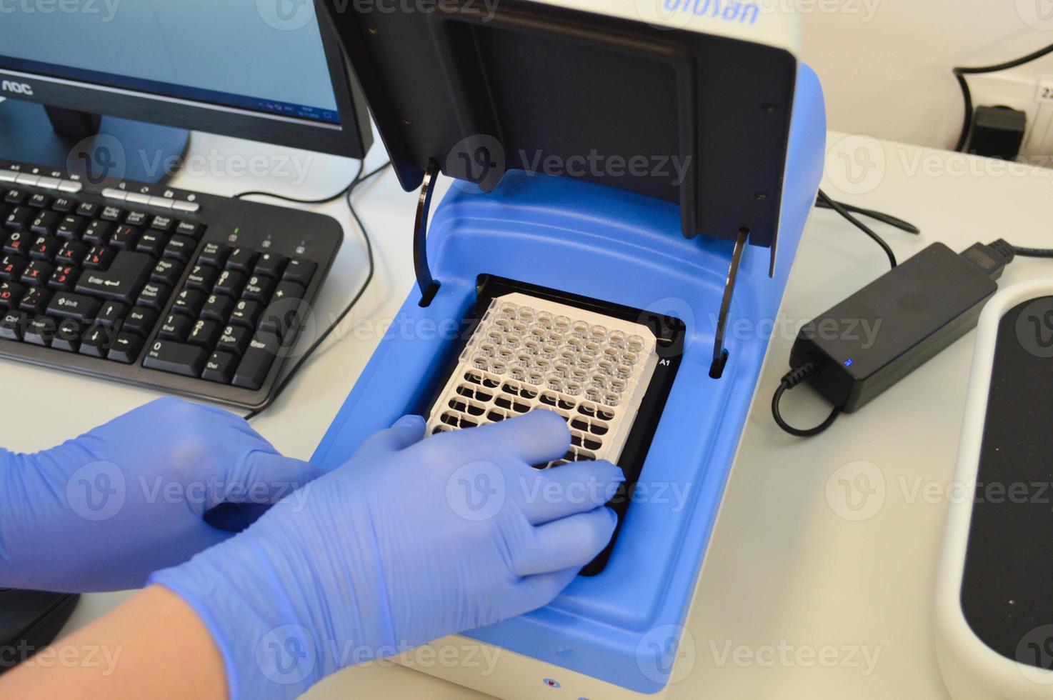 a doctor in a blue sterile glove puts a plate with a reagent into the apparatus to perform the study. laboratory analyzer. venous blood test photo