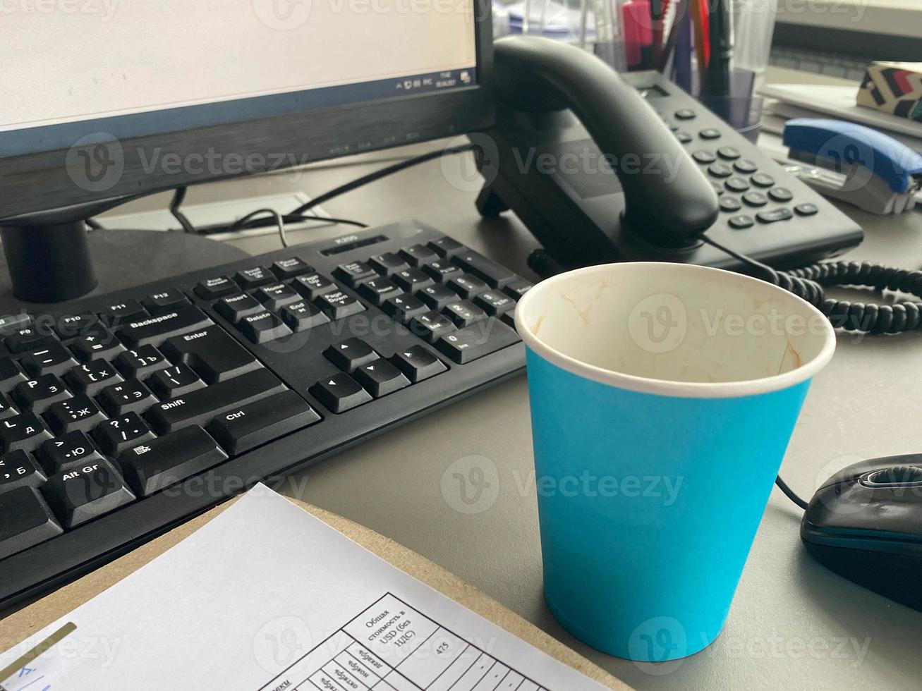 Cardboard blue coffee cup from a coffee shop on a desktop with a computer with a keyboard and mouse and office supplies of an office worker during lunch. Business coffee break photo