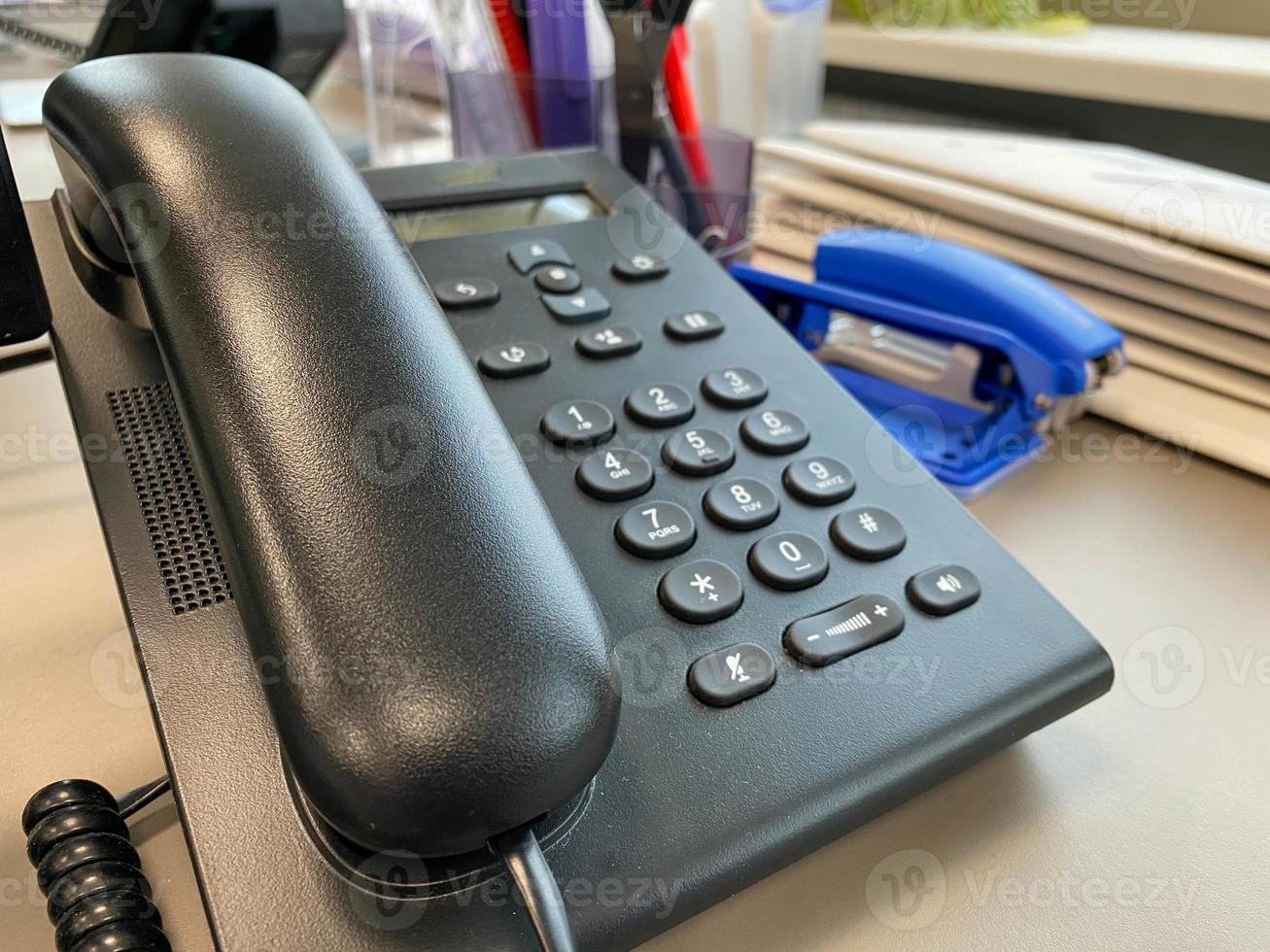 Black plastic office landline corded telephone with a handset and buttons for solving business problems and making calls for negotiations photo