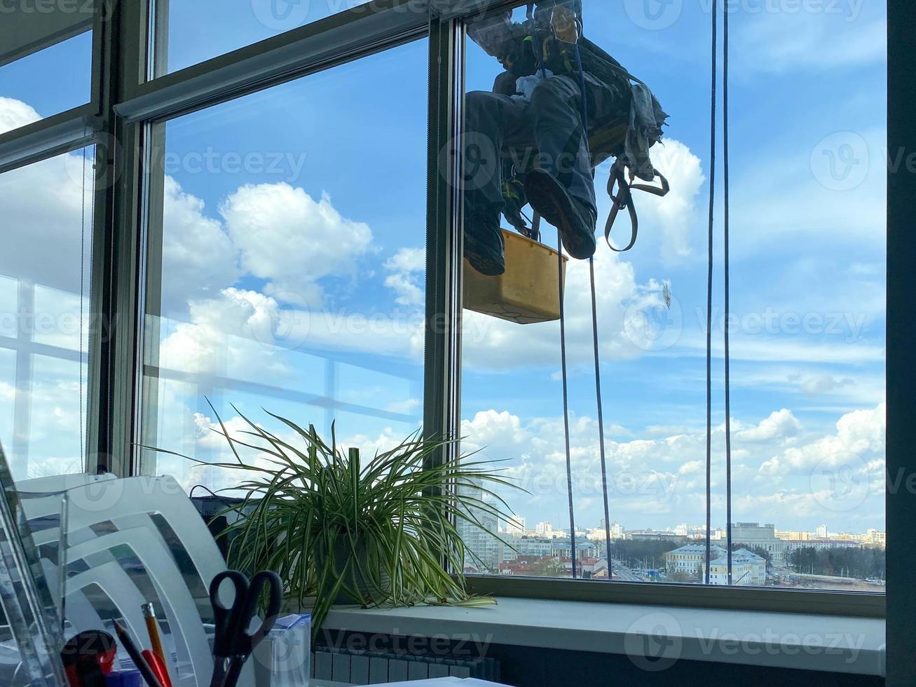 A male window washer worker, industrial climber hangs on a tall building, skyscraper and washes large glass windows for cleanliness high above a large city in an office business building photo