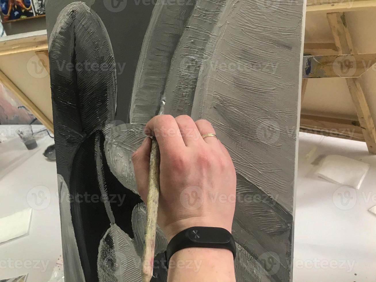 An artist's hand paints a black and white creative picture with a brush on canvas in a workshop photo