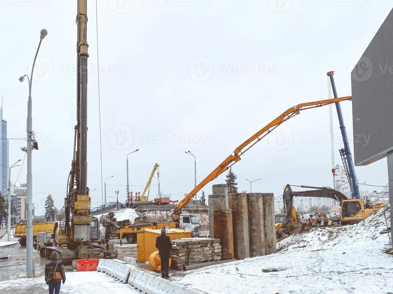 construction of a bridge in the city center in winter under snow. machines for mixing concrete and creating asphalt. construction of large concrete structures photo