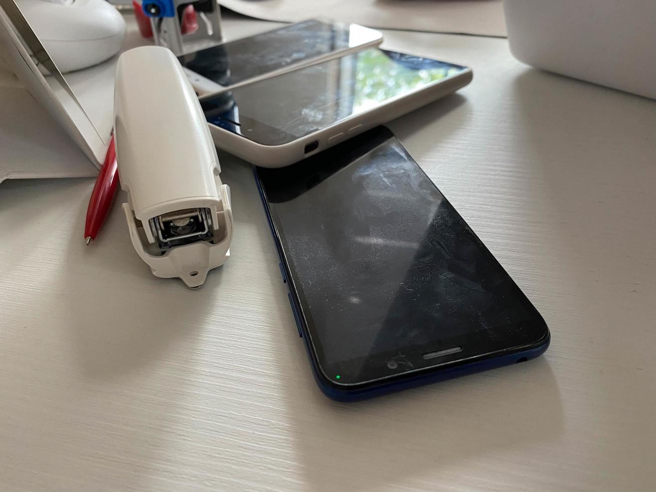 dos teléfonos móviles con pantalla táctil que funcionan, los teléfonos inteligentes se encuentran sobre la mesa en la oficina con papelería, una grapadora, un sello y una computadora portátil foto
