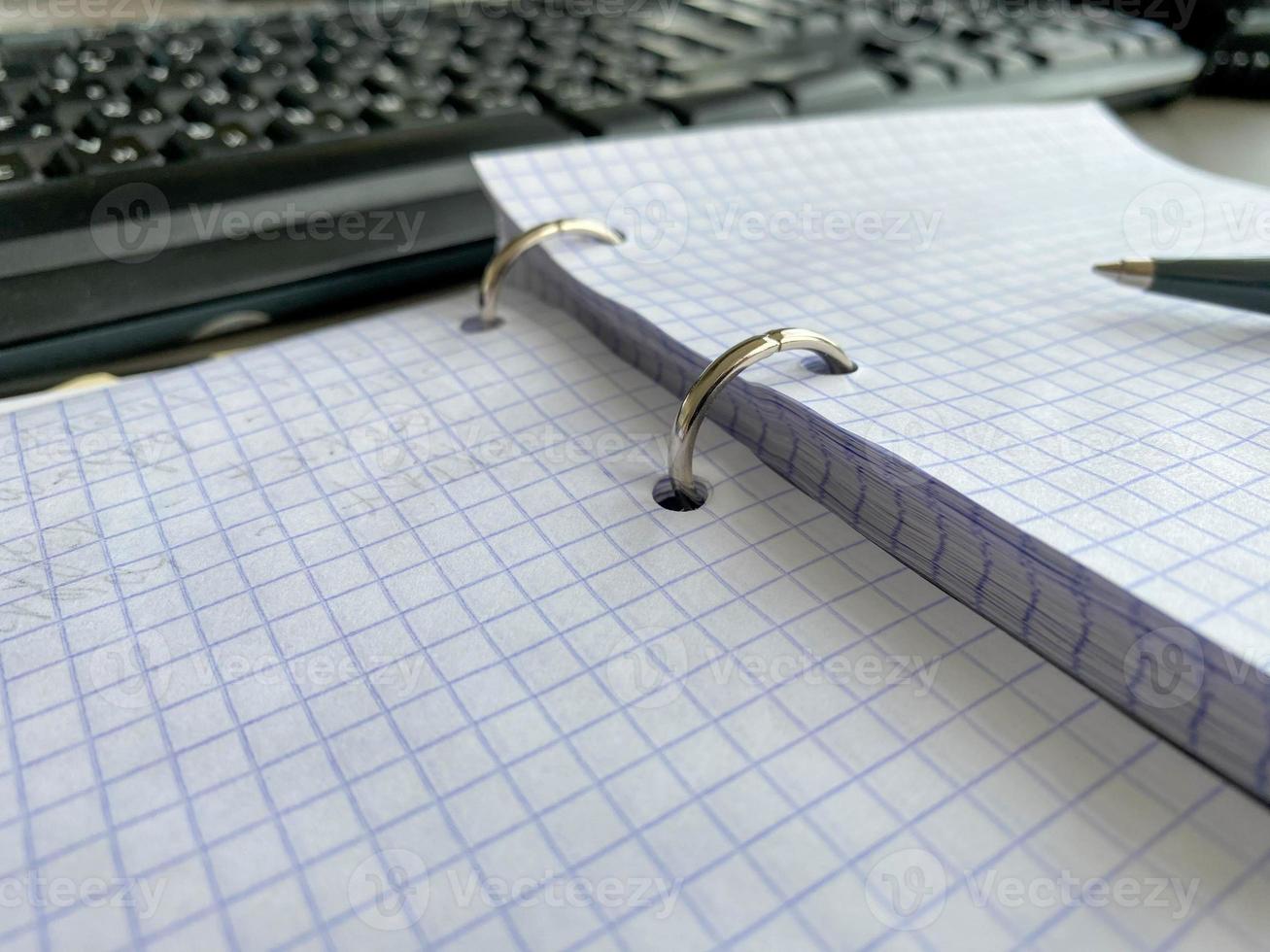 One paper notepad with spiral binder and blank sheets near black plastic pen lies of blue office table. Top view. Copy space for photo