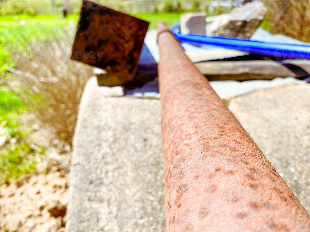 los accesorios oxidados yacen en el campo. un palo de metal yace en el suelo y está cubierto de corrosión. una pieza vieja, oxidada y sucia de una valla innecesaria. base de la antigua puerta del pueblo foto