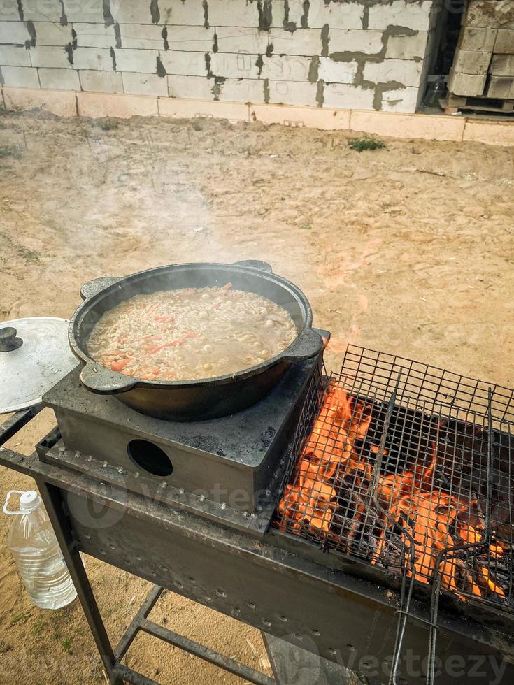cooking on an open fire. a fire is lit on the grill and there is a cauldron with pilaf, next to it lies a barbecue grill. outdoor meals. rice pilaf photo