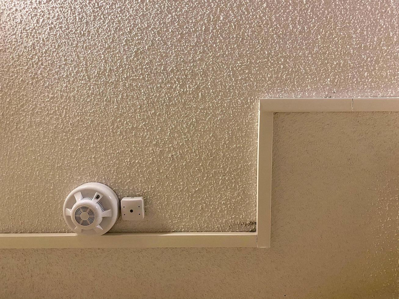 White plastic small fire detector smoke detector with alarm on the ceiling in the entrance. The background photo