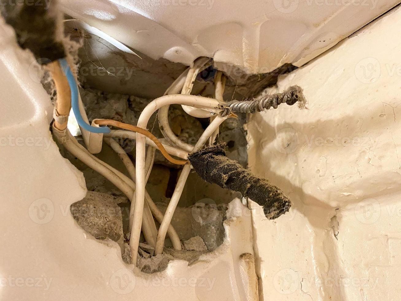 viejos cables retorcidos enredados en telarañas y polvo en un agujero en una pared en un sitio de construcción. electricista industrial muy pobre foto