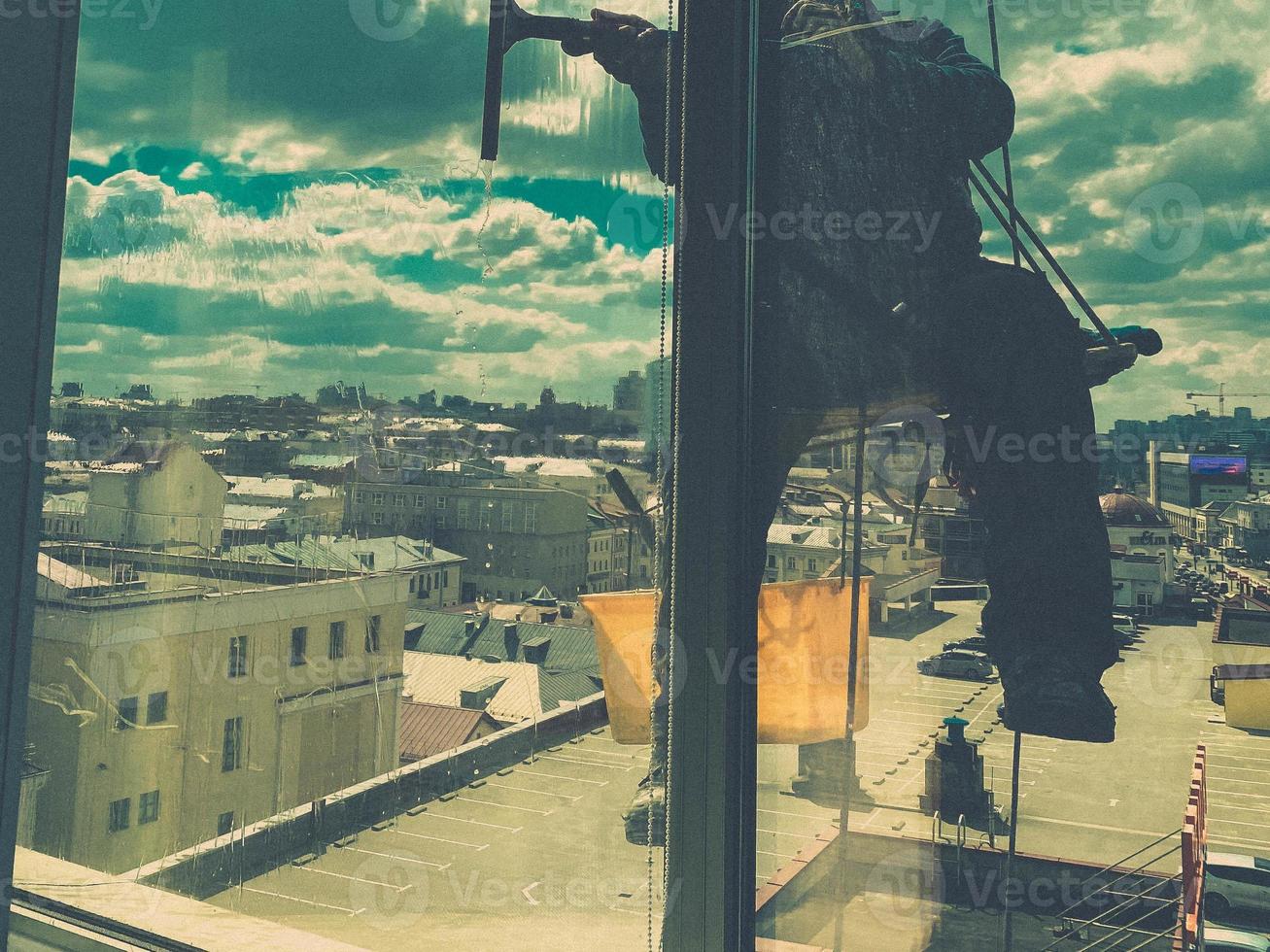 Industrial climber window cleaner in helmet and gloves washes windows on tall building top view camera movement photo