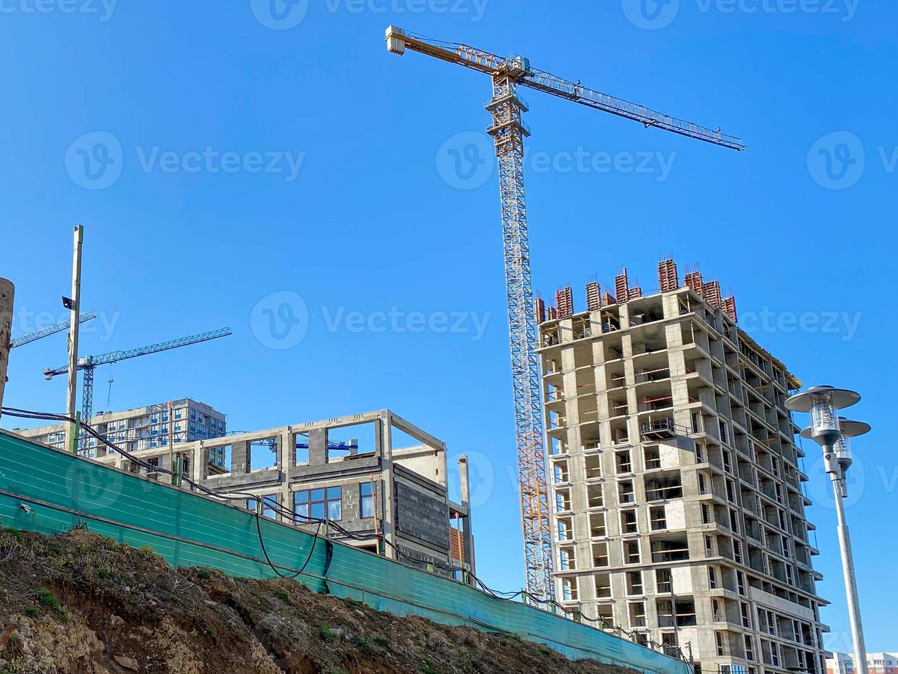 colocación de losas de pavimento y bordes en el sitio de construcción. grúas torre en acción con maquinaria y constructores. grúa construir el edificio de gran altura. nuevo rascacielos residencial. proyecto de reforma de casa alta foto