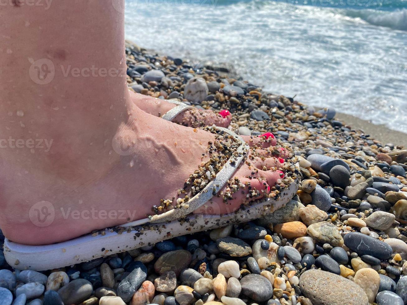 Female legs, feet in rubber slippers with a beautiful red pedicure on the background of sand on vacation on the beach in a warm tropical eastern paradise country southern resort photo