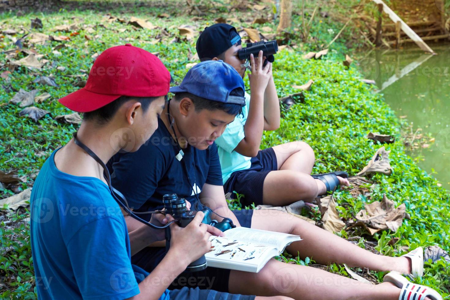 un niño asiático y sus amigos se invitan a ver pájaros en el bosque comunitario durante las vacaciones. y ayúdense unos a otros a buscar los tipos de aves que se encuentran en la guía de aves. foto