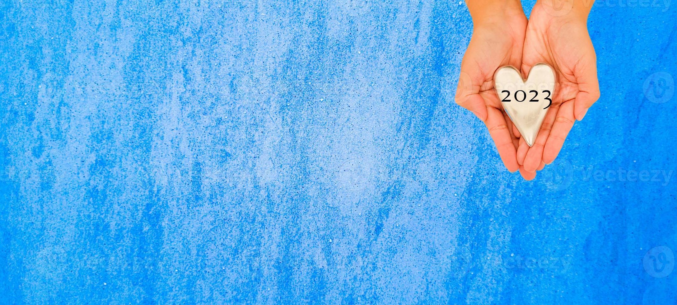 heart being held by female hand written 2023 with wood background,happy new year 2023 photo