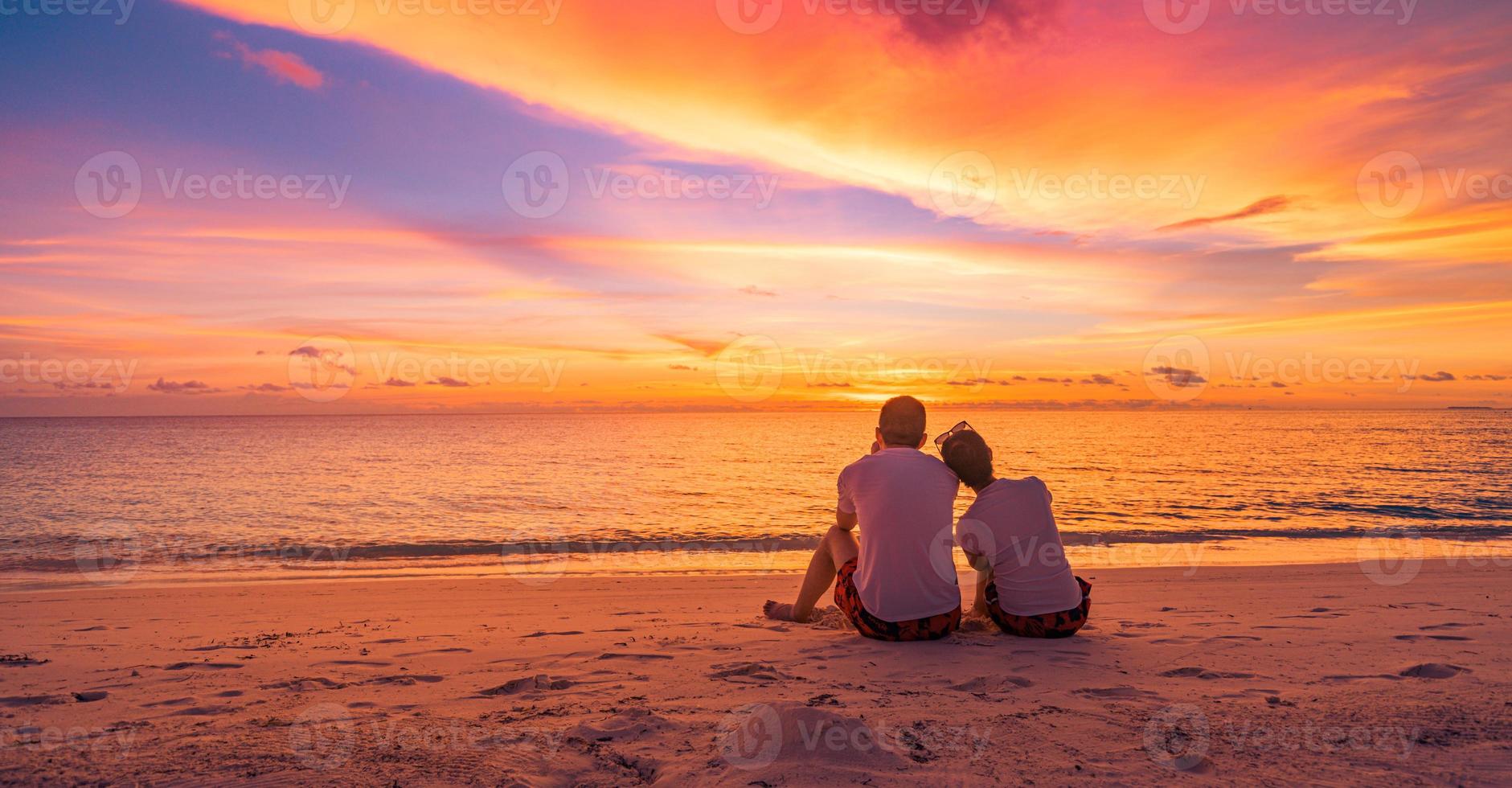 Love couple watching sunset together on beach travel summer holidays. People silhouette from behind sitting enjoying view sunset sea tropical island, destination vacation. Romantic freedom lifestyle photo