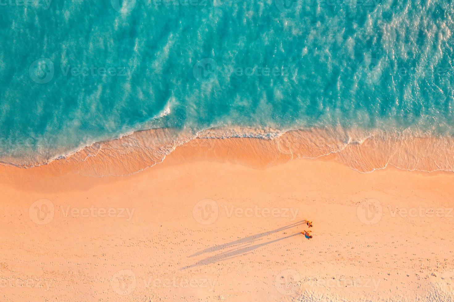 Aerial view of amazing beach with couple walking in sunset light close to turquoise sea. Top view of summer beach landscape, romantic inspirational couple vacation, romantic holiday. Freedom travel photo