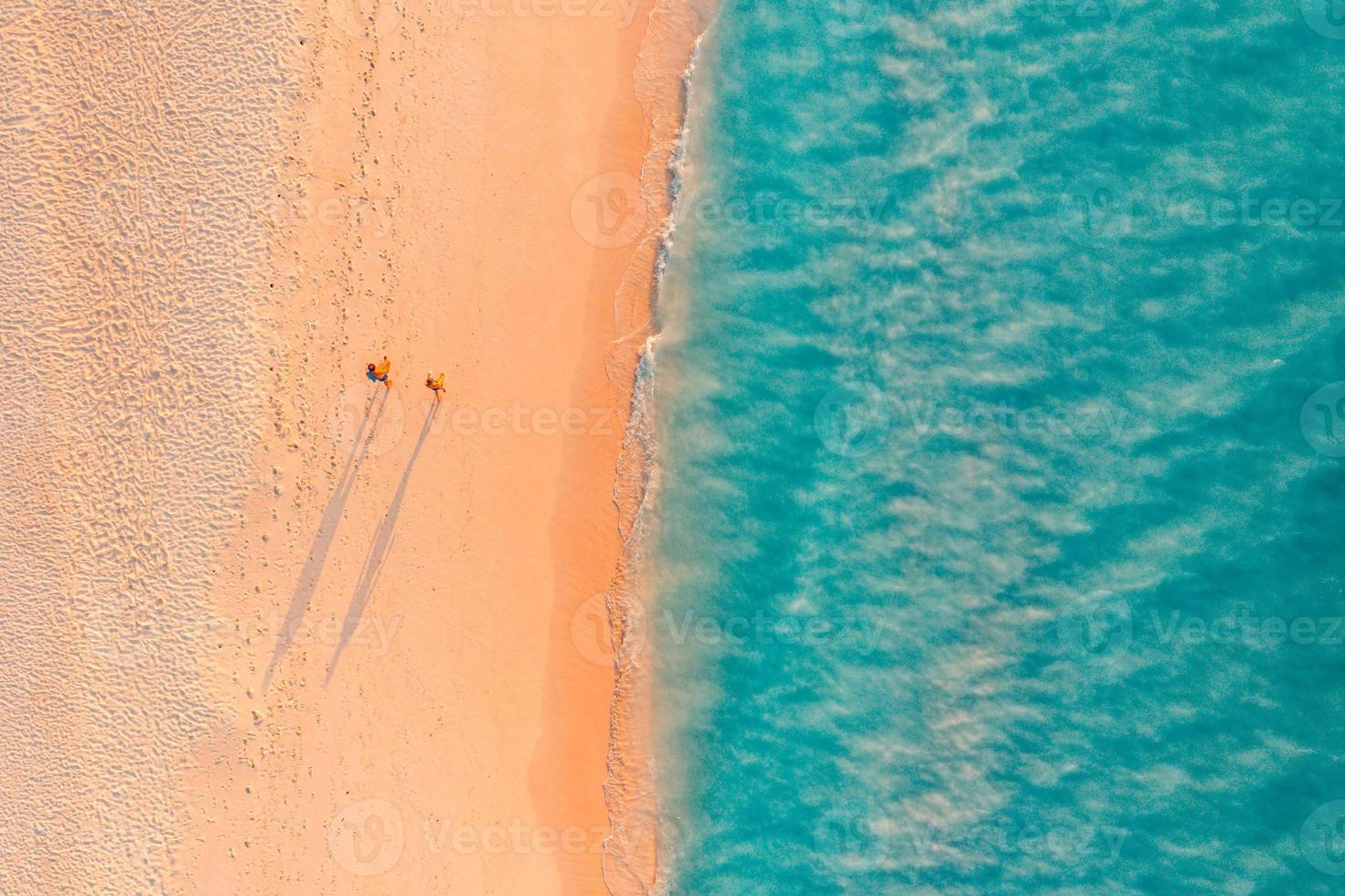 vista aérea de una playa increíble con una pareja caminando a la luz del atardecer cerca del mar turquesa. vista superior del paisaje de la playa de verano, vacaciones románticas en pareja, vacaciones románticas. viajes de libertad foto