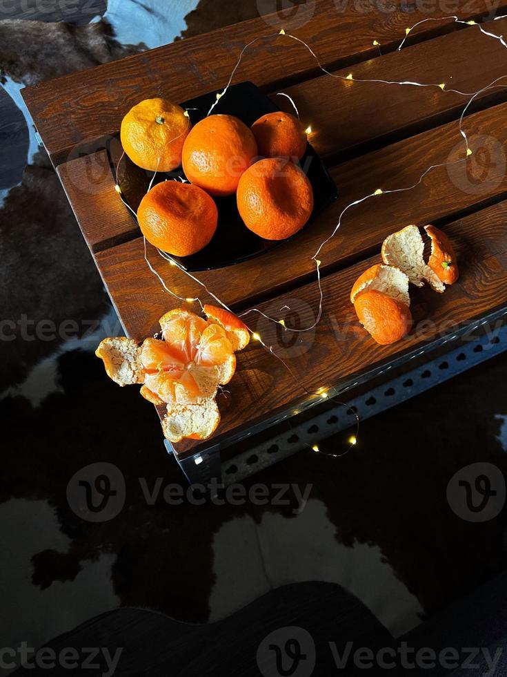 mandarinas abiertas y enteras sobre una mesa de madera con el telón de fondo de las luces navideñas y una alfombra de piel de vaca foto