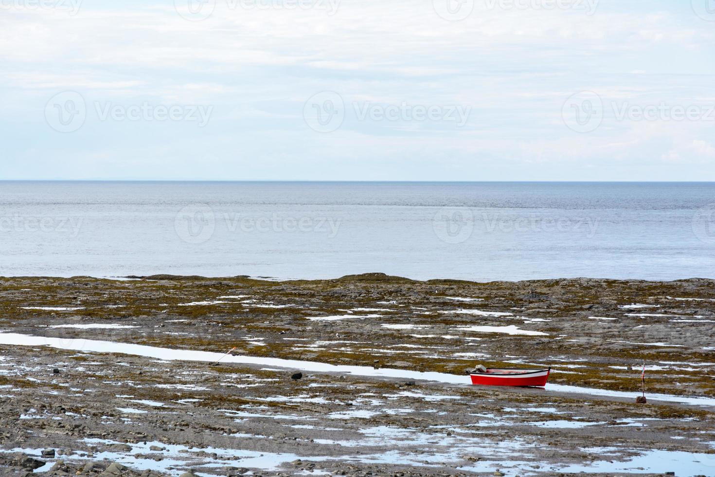 Red boat in the Gaspesie peninsula in Canada between the sea and beautiful landscapes in during a summer day photo