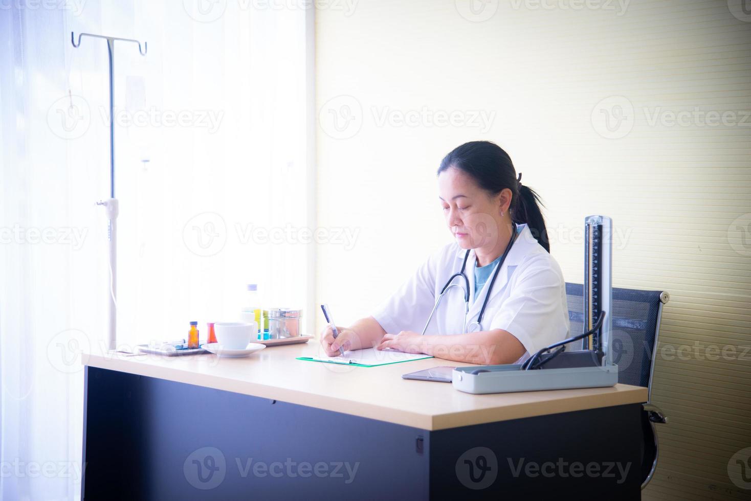 una doctora con dispositivos médicos está revisando la salud del paciente y tomando nota del libro blanco en el hospital, que es el negocio de la salud foto