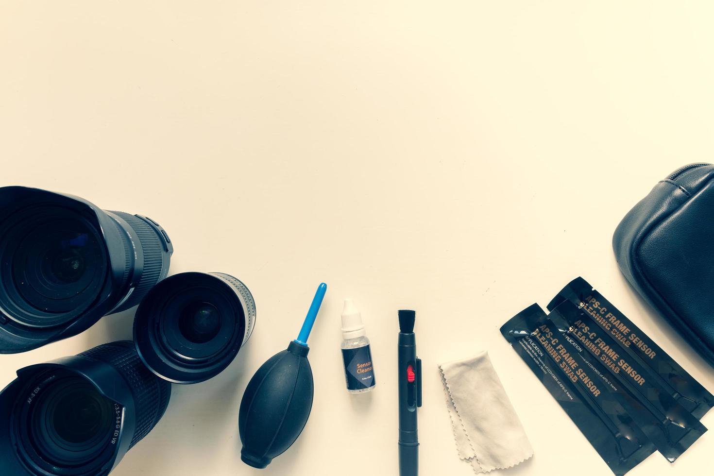 Dlsr lenses, filters, swabs, sensor cleaner, air blower, microfiber and lens pen knolled on a textured yellow background.Cleaning set for photographic equipment maintenance photo