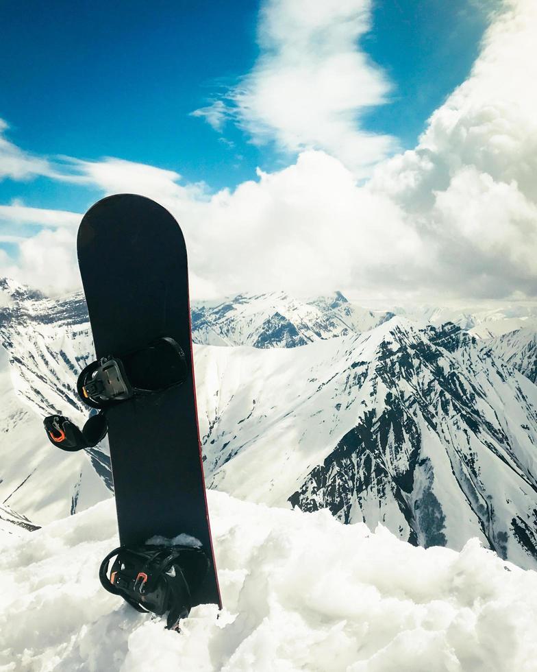 una tabla de snowboard negra en la nieve con montañas blancas al fondo. concepto de fin de temporada de esquí.gudauri. sakartvelo. panorama de vacaciones de invierno de georgia foto