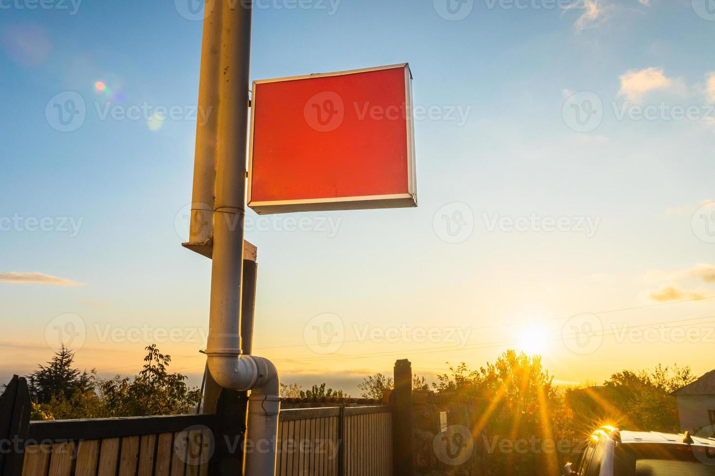 Blank red plastic signboard on post. Empty mounted sign plate mock up.Red outdoor plexiglass signage for hotel or store info mockup template. Red copy space sign board and sunburst photo