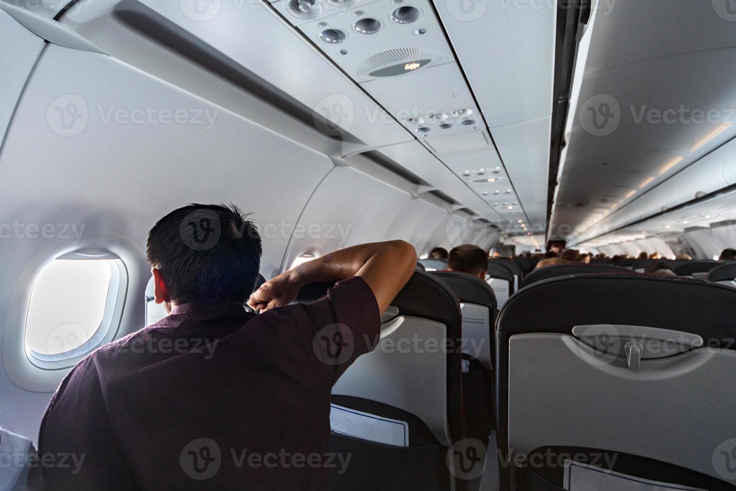 Man looks in airplane window. New aircraft cabin with comfortable seats. Economy class flight of new airline without flight delay. photo